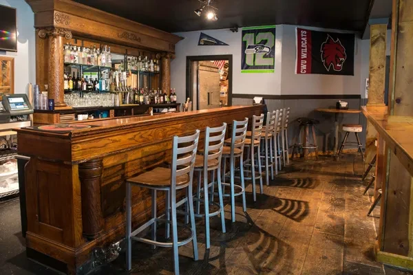 Ornate wooden bar with liquor bottles, bar stools, and sports flags.
