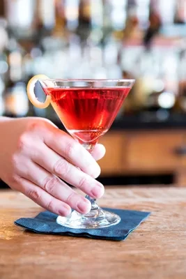 Red cocktail with lemon peel, held by hand on bar counter.