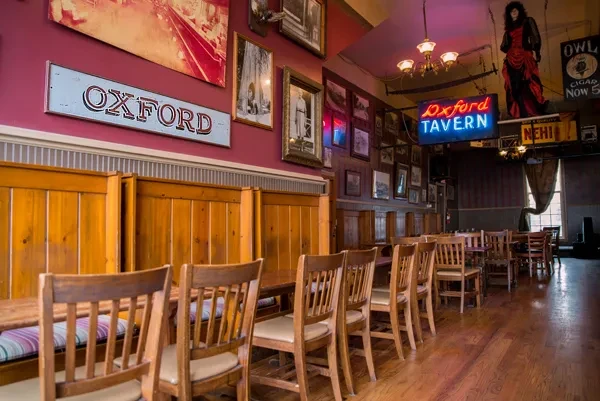 Rustic Oxford Tavern interior with wooden seating, maroon walls, framed art.