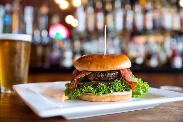 Gourmet burger with bacon, cheese, lettuce, and beer in a bar.