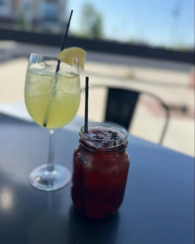 Two drinks: yellow in wine glass, red in mason jar, outdoors.