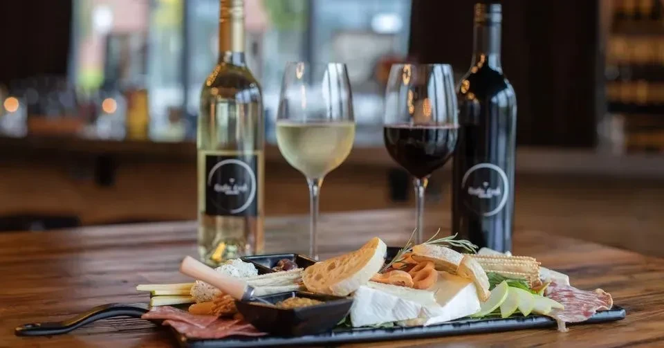 Rustic charcuterie board with cheeses, meats, and two wines.