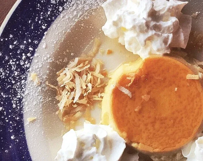 Close-up of caramelized flan with whipped cream and toasted coconut.