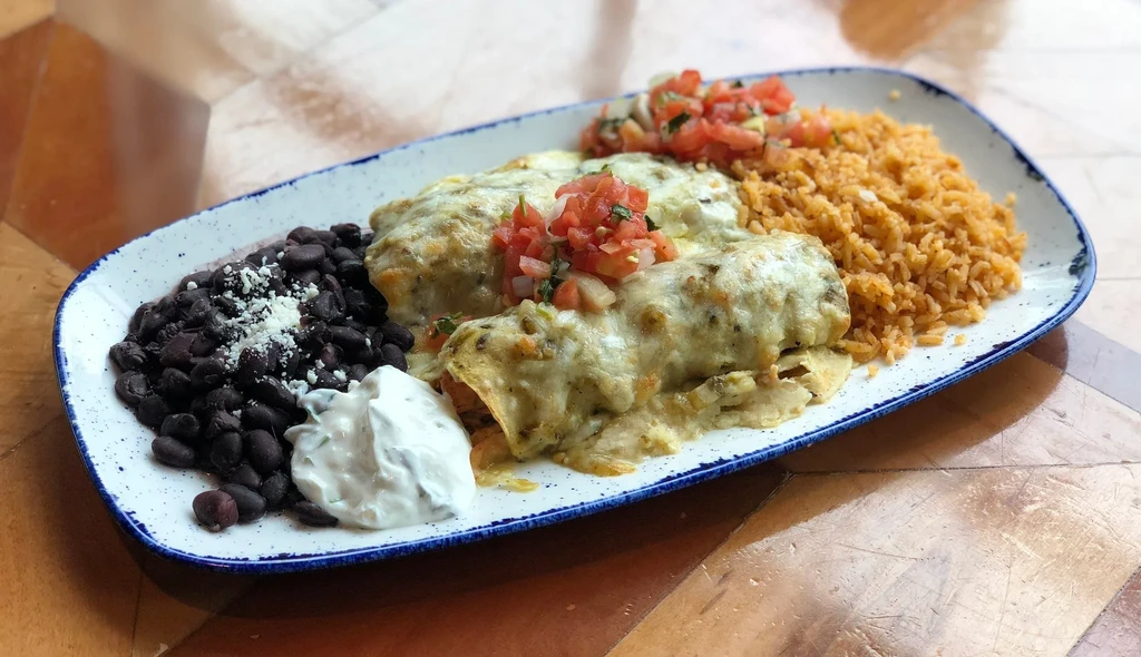 Enchiladas with melted cheese, green sauce, Mexican rice, and black beans.