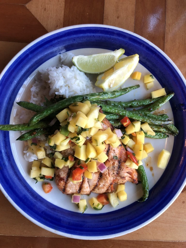 Grilled fish, mango salsa, rice, and green beans on a striped plate.