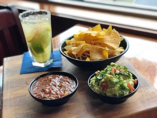 Margarita, tortilla chips, salsa, and guacamole on a wooden table.