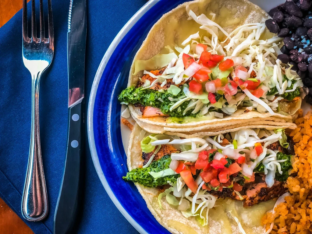Overhead: Two tacos, rice, and black beans on a blue-rimmed plate.