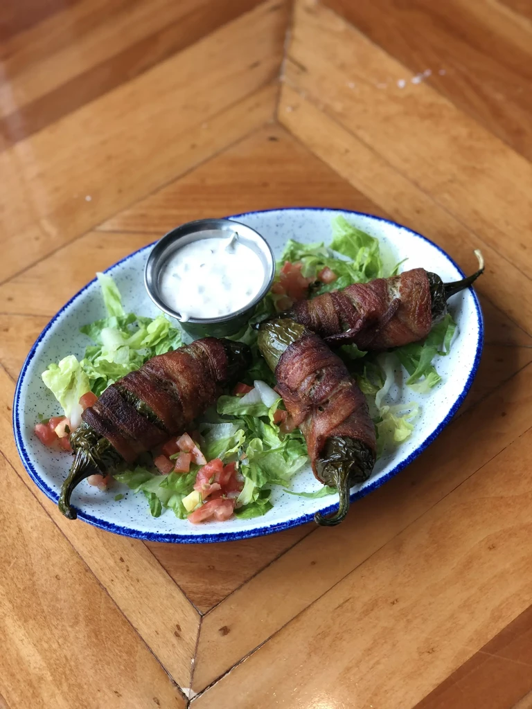 Bacon-wrapped stuffed peppers with lettuce, tomatoes, and dipping sauce.