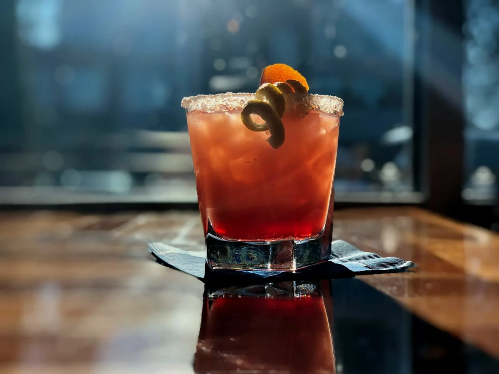 Vibrant cocktail, ice, citrus peels, and a white granular rim.