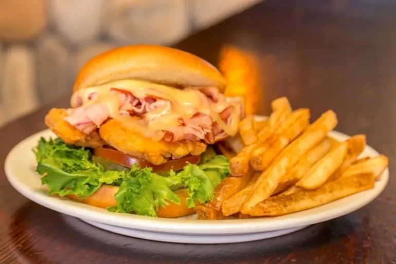 Fried chicken sandwich with ham, melted cheese, and fries on a plate.