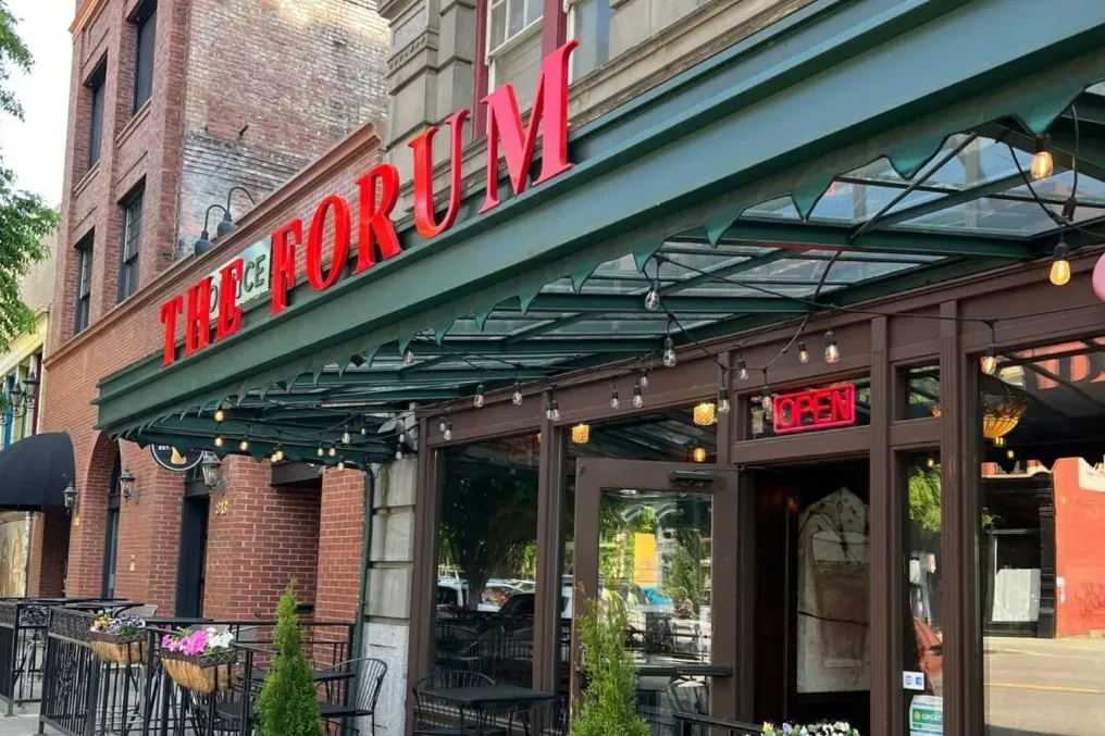 The Forum restaurant: brick building, green awning, outdoor seating, 'OPEN' sign.