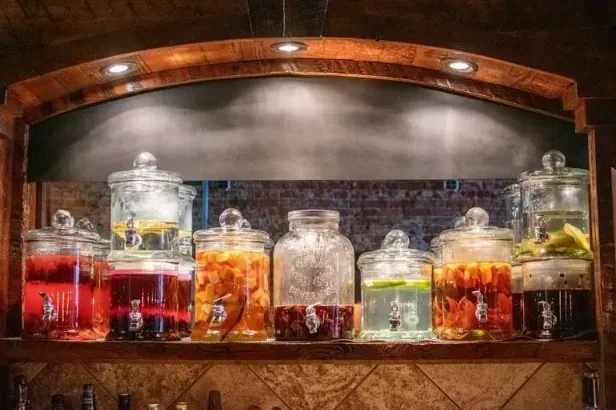 Glass dispensers with various fruit-infused beverages on a restaurant shelf.