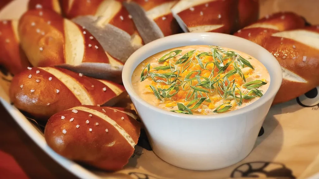 Soft pretzel sticks with salt arranged around a cheesy orange dip.