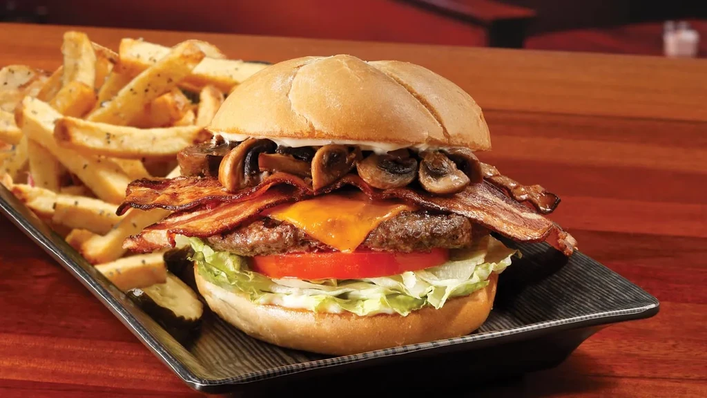 Fully loaded gourmet burger, fries, and pickles on a rectangular plate.