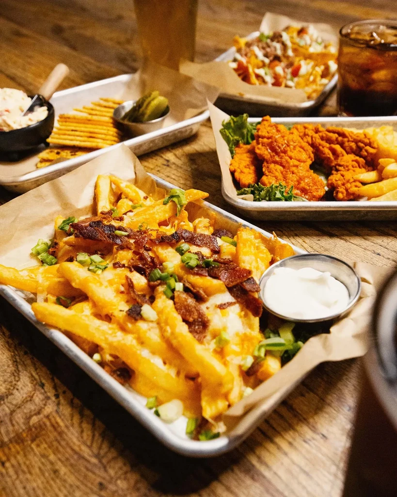 Loaded fries, chicken, nachos, and drinks on a rustic wooden table.