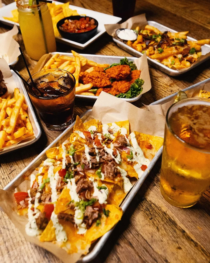 Overhead view of nachos, chicken wings, fries, and multiple drinks.