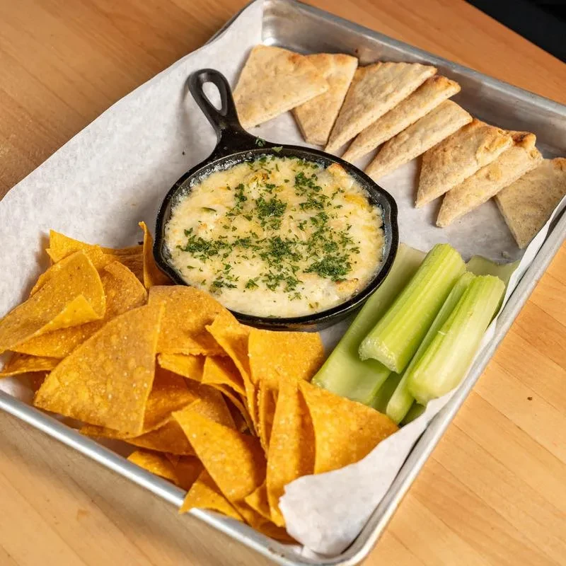 Cast iron skillet with cheesy dip, tortilla chips, pita, and celery.