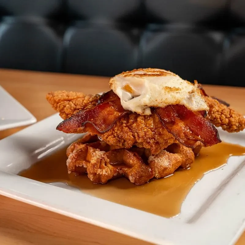 Chicken and waffles with bacon, fried egg, and syrup.