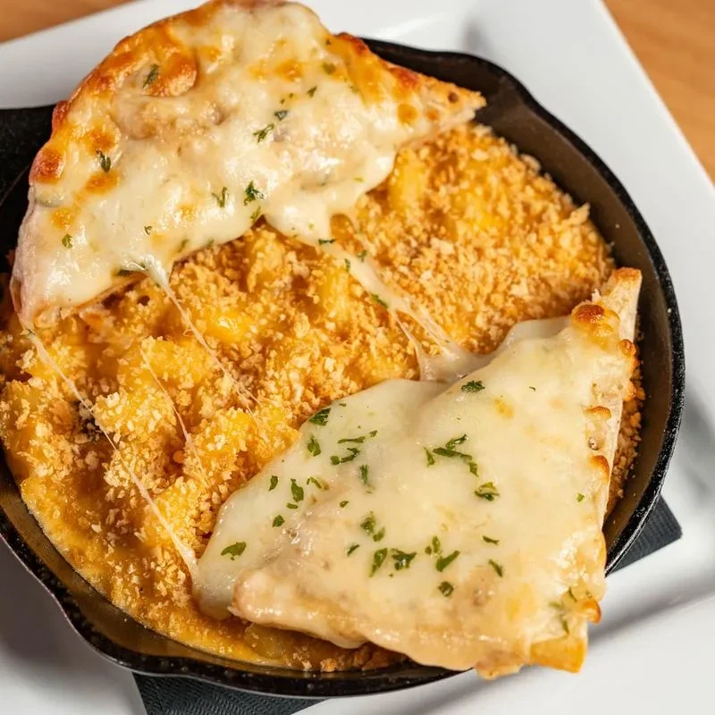 Cheesy baked mac and cheese with garlic bread in cast iron skillet.