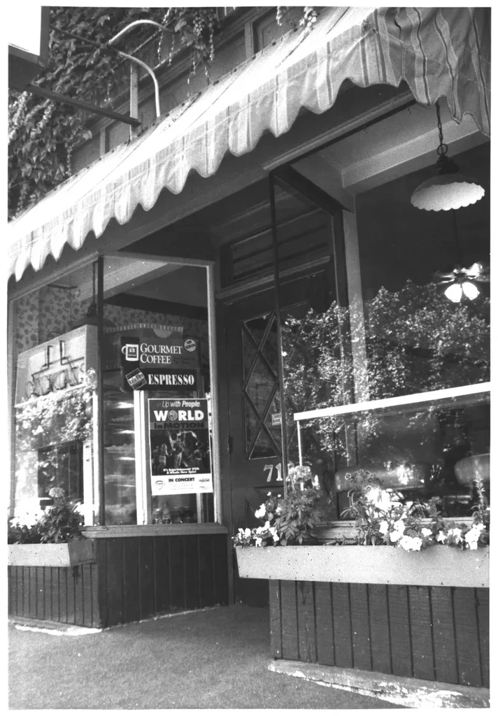 Black and white cafe storefront with striped awning and coffee signs.