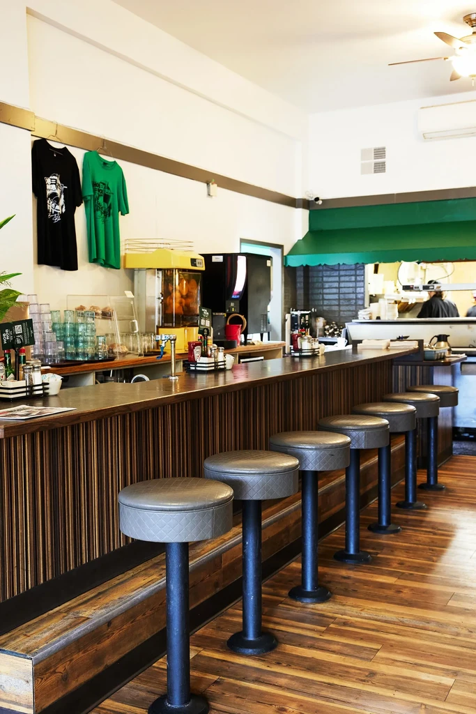Casual diner interior with a long wooden counter and six gray stools.