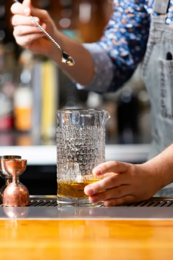 Bartender's hands stirring an amber drink in a mixing glass.