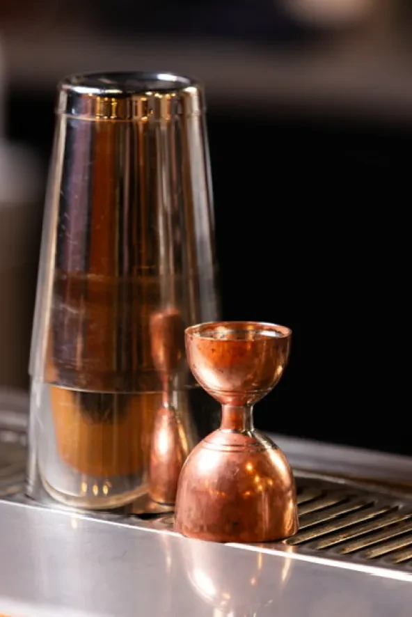 Polished Boston shaker and copper jigger on a ribbed stainless steel surface.