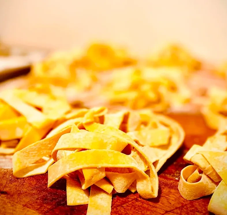 Piled fresh golden pasta, floured, on a wooden surface.