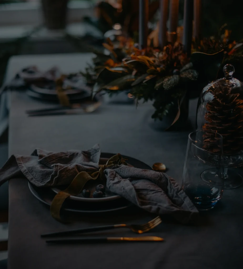 Low-light elegant table setting with napkin, berries, modern cutlery, pinecone cloche.