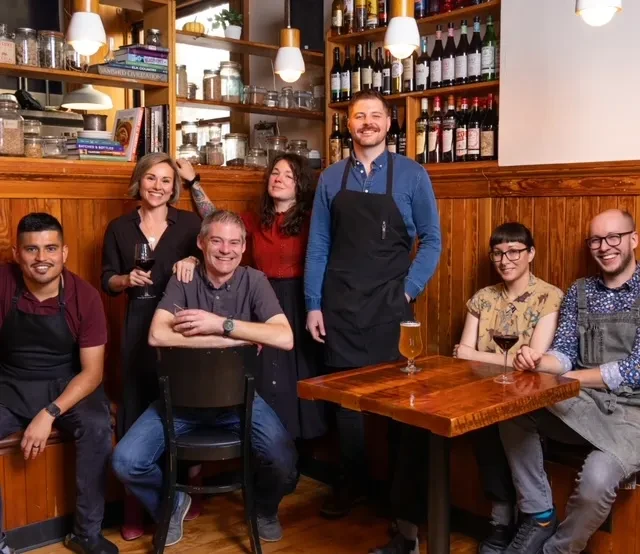 Seven smiling restaurant staff pose in a cozy wooden interior.