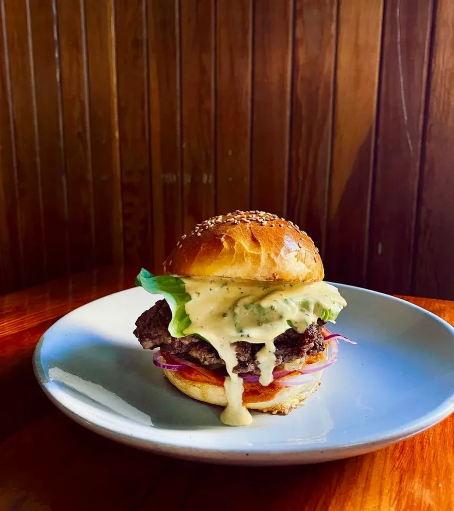 Substantial hamburger with lettuce, onion, and creamy herb sauce on plate.