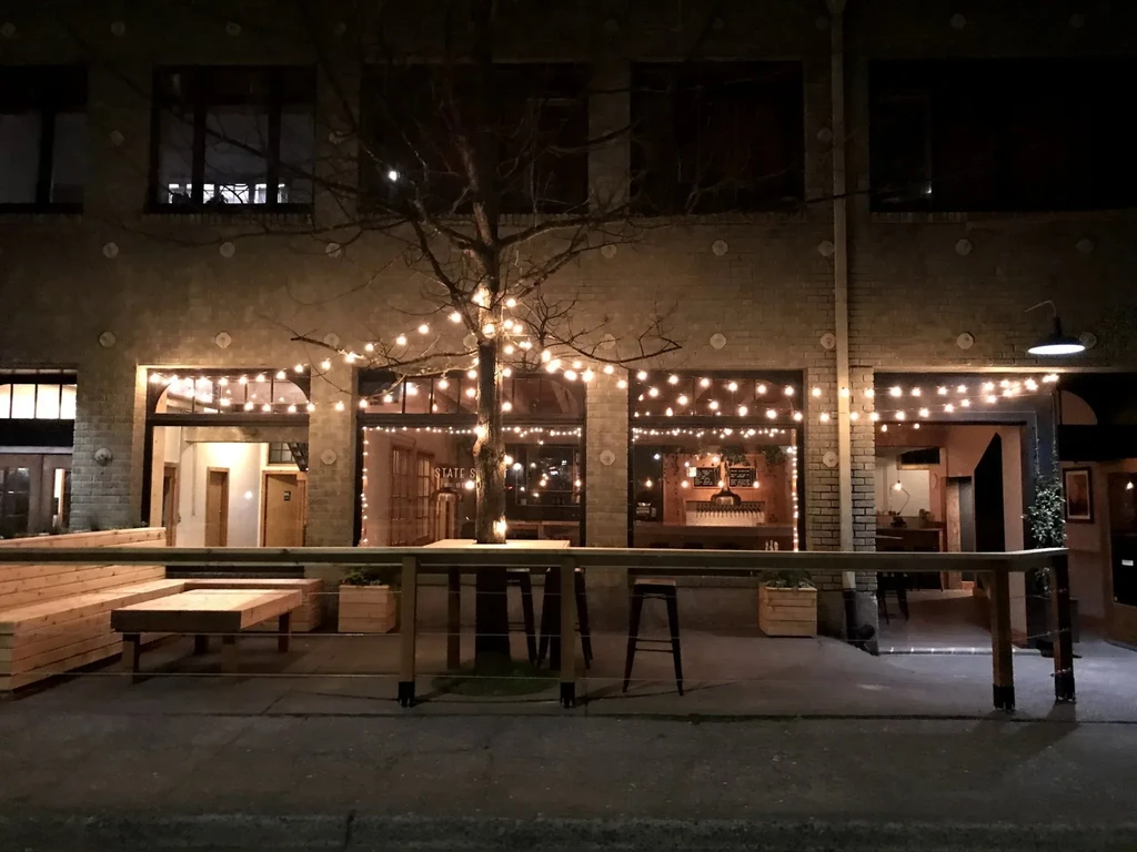 Brick building, patio, and tree lit by warm string lights at night.