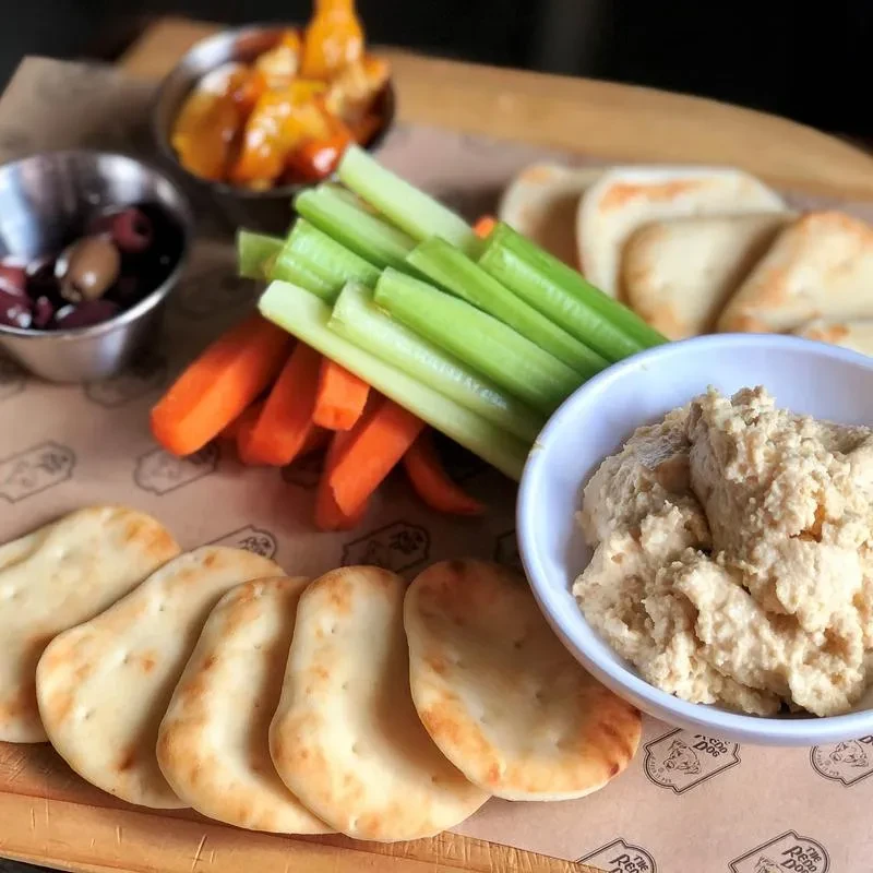 Appetizer platter with hummus, pita bread, celery, carrots, and olives.