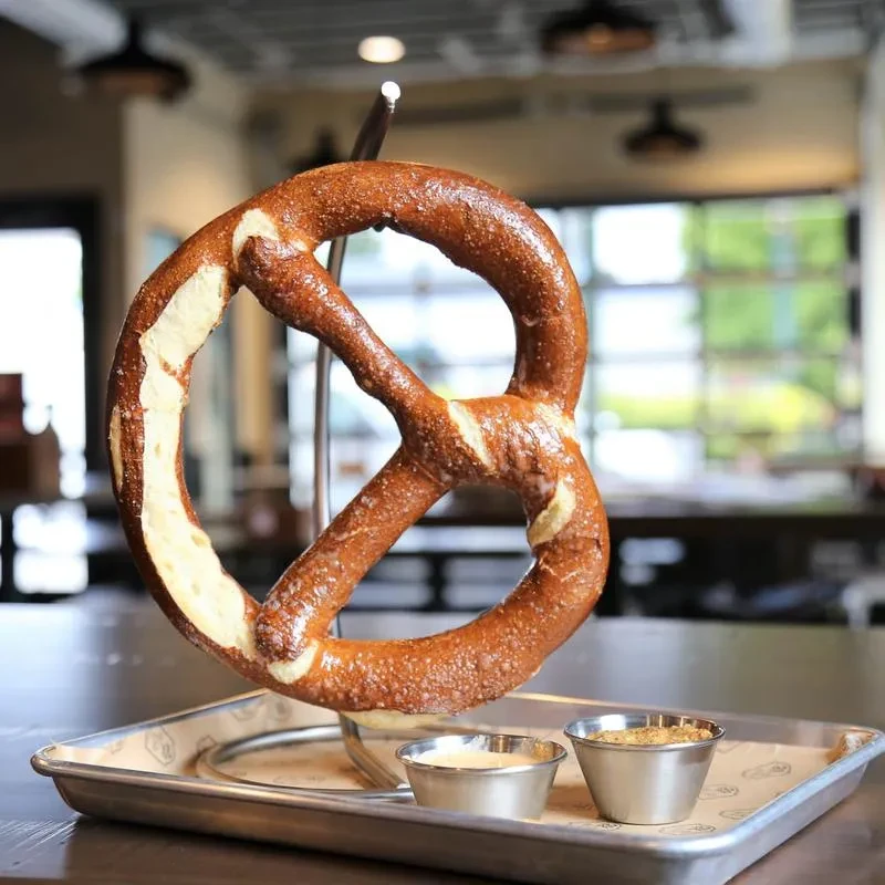 Large, golden-brown pretzel, salt, two dipping sauces on silver tray.