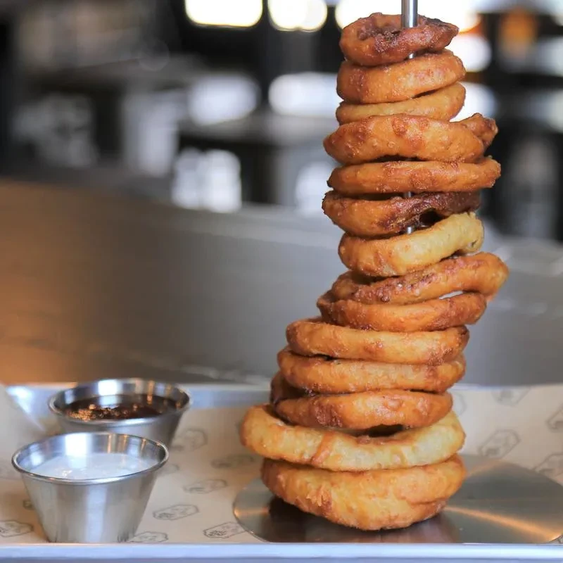 Stack of golden-brown onion rings skewered with dark and white sauces.