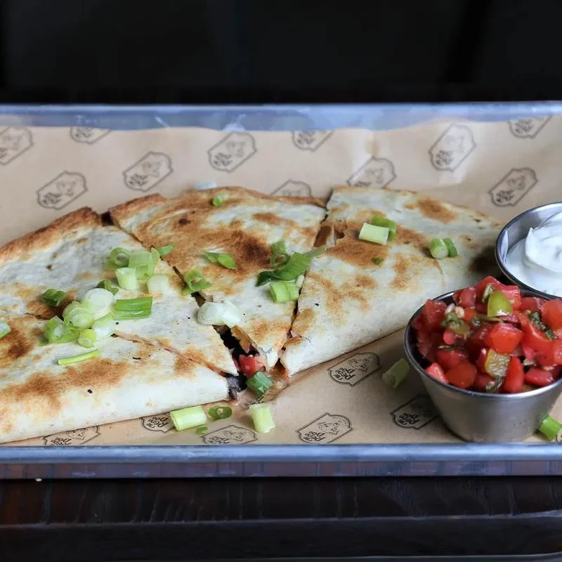 Close-up of a quesadilla with green onions, salsa, and sour cream.