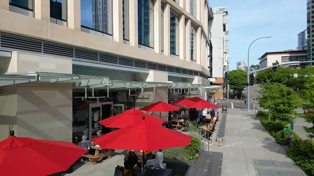 Sunny urban patio with bright red umbrellas and seated diners.