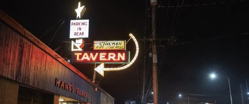 Night scene of a rustic tavern with neon "TAVERN" sign and arrow.