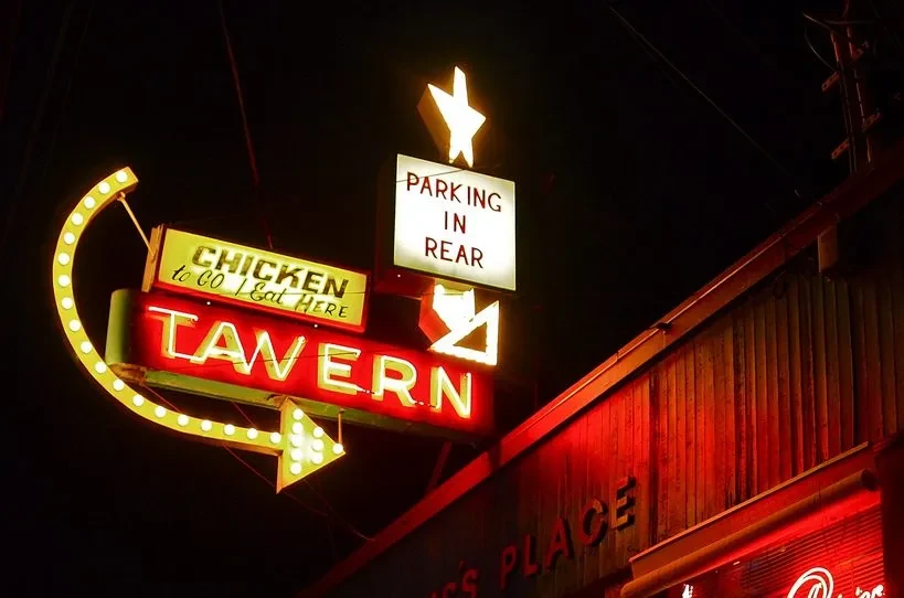 Glowing red 'TAVERN' and yellow 'CHICKEN to GO' neon signs at night.
