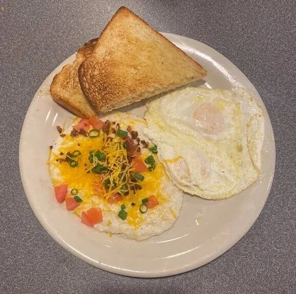 Breakfast plate: toast, fried eggs, and grits topped with cheese, tomatoes.
