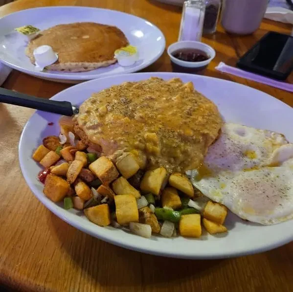 Two plates of eggs, home fries, savory item, and pancakes.