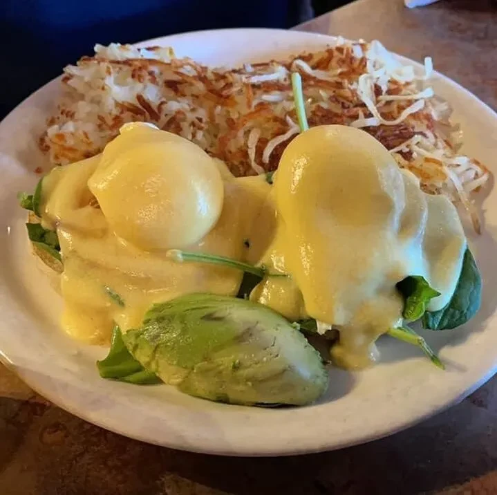 Eggs Benedict with hollandaise, spinach, avocado, and crispy hash browns.