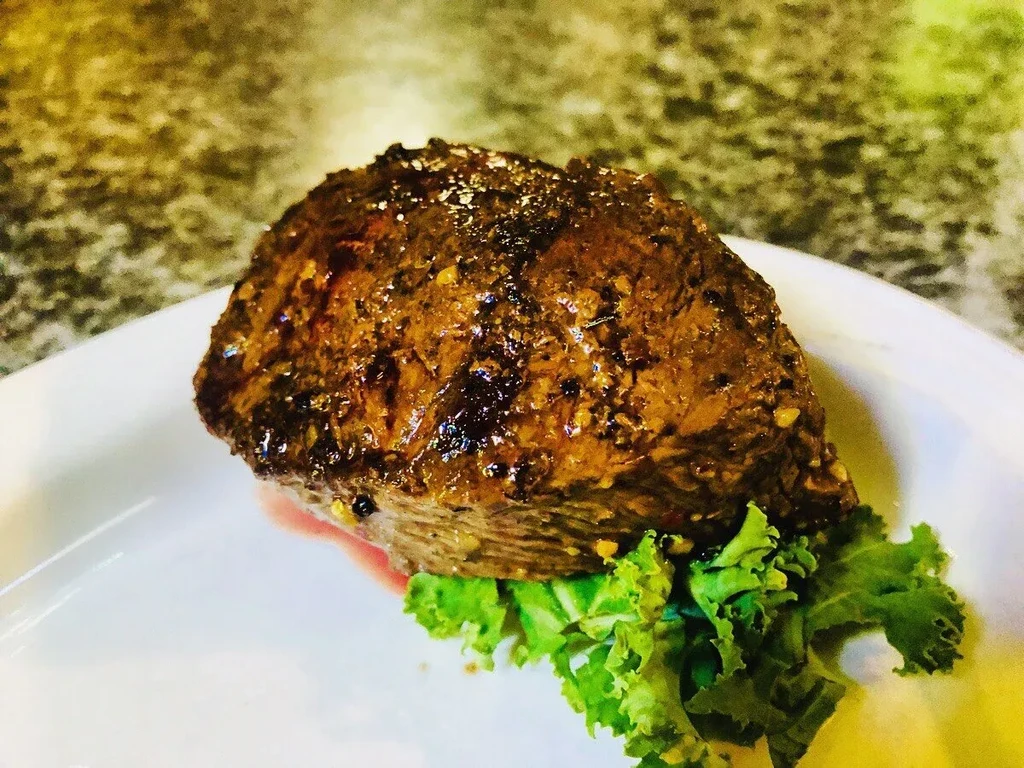 Close-up of seared, seasoned meat on a white plate with greens.