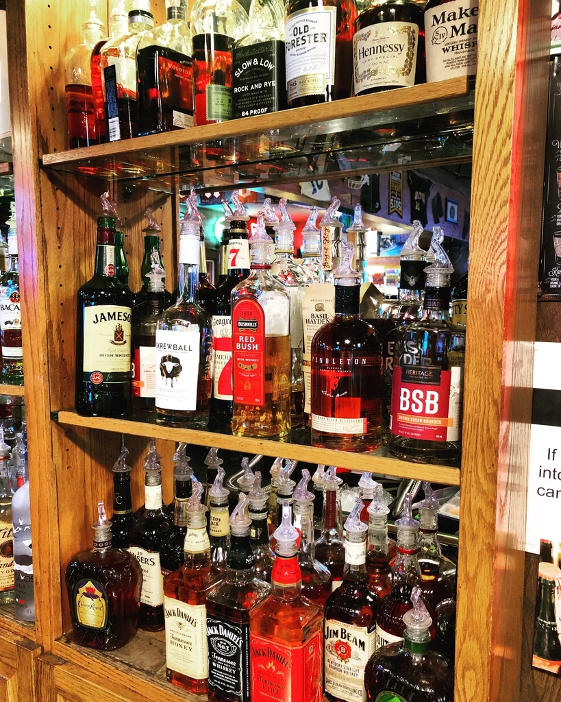 Well-stocked bar shelves display various liquor bottles with pour spouts.
