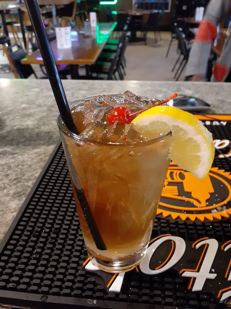 Iced amber cocktail with cherry, sugared lemon, straw on bar mat.