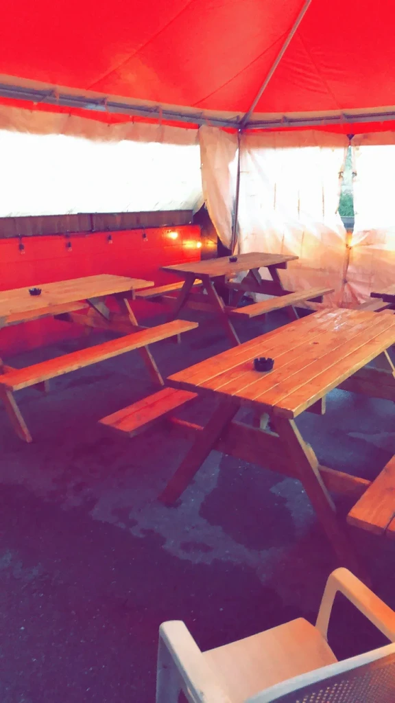 Red tent covers empty patio with wooden picnic tables and string lights.
