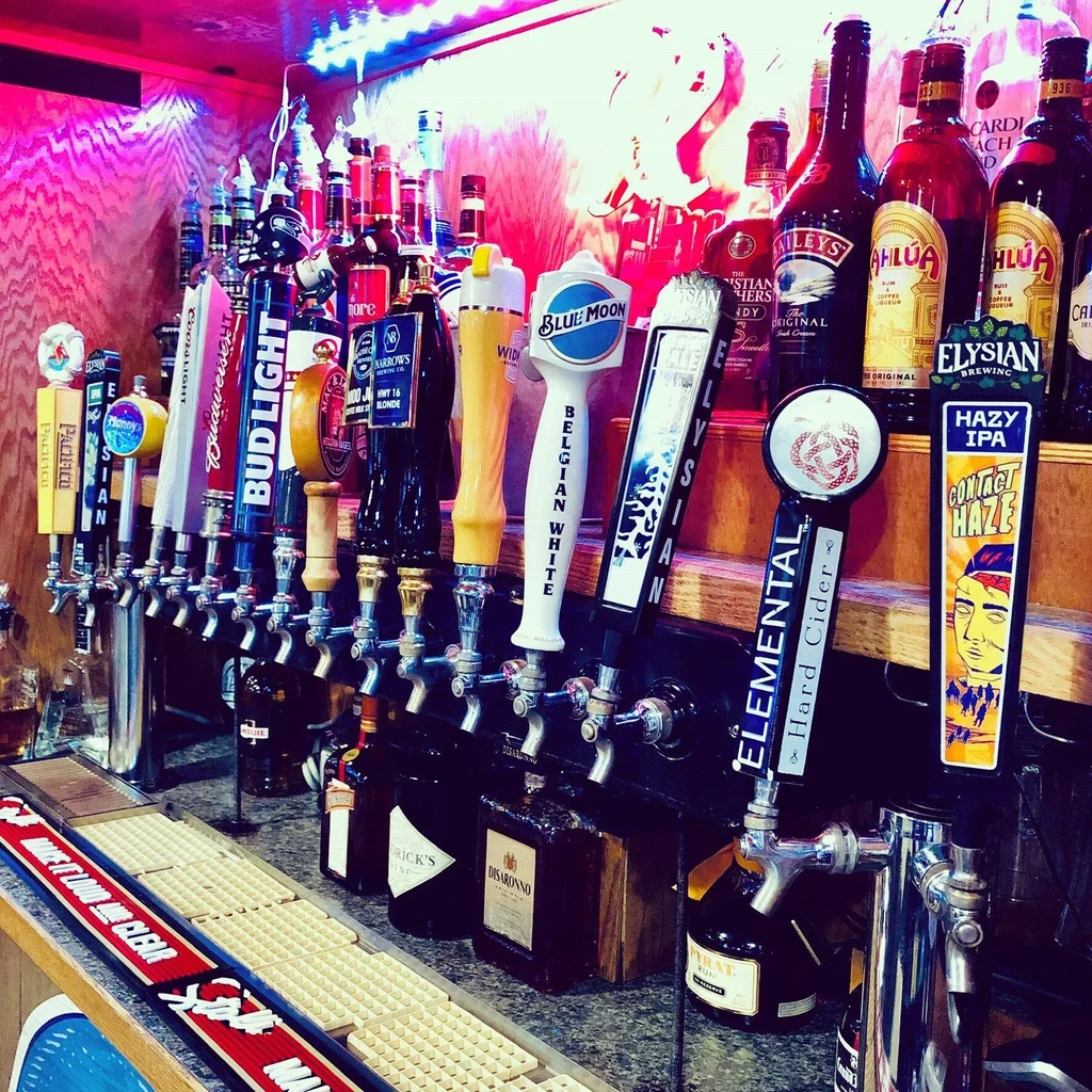 Rows of branded beer taps and liquor bottles under colorful neon light.
