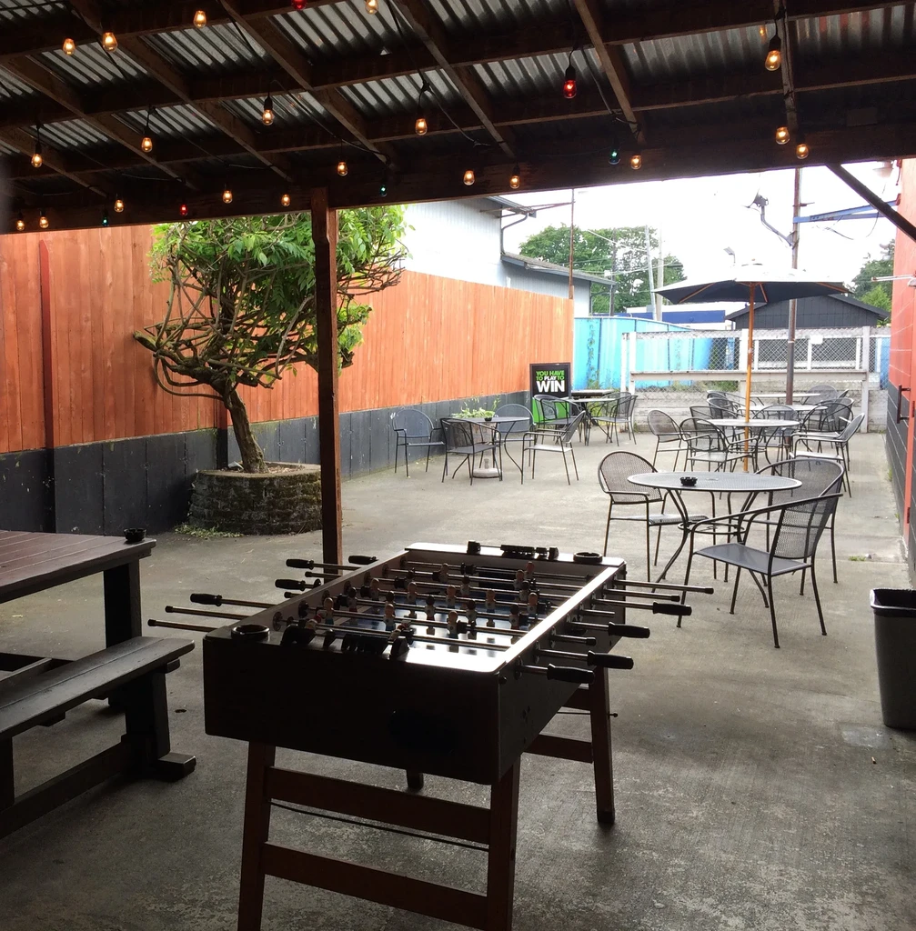 Outdoor patio features foosball table under colorful string lights.