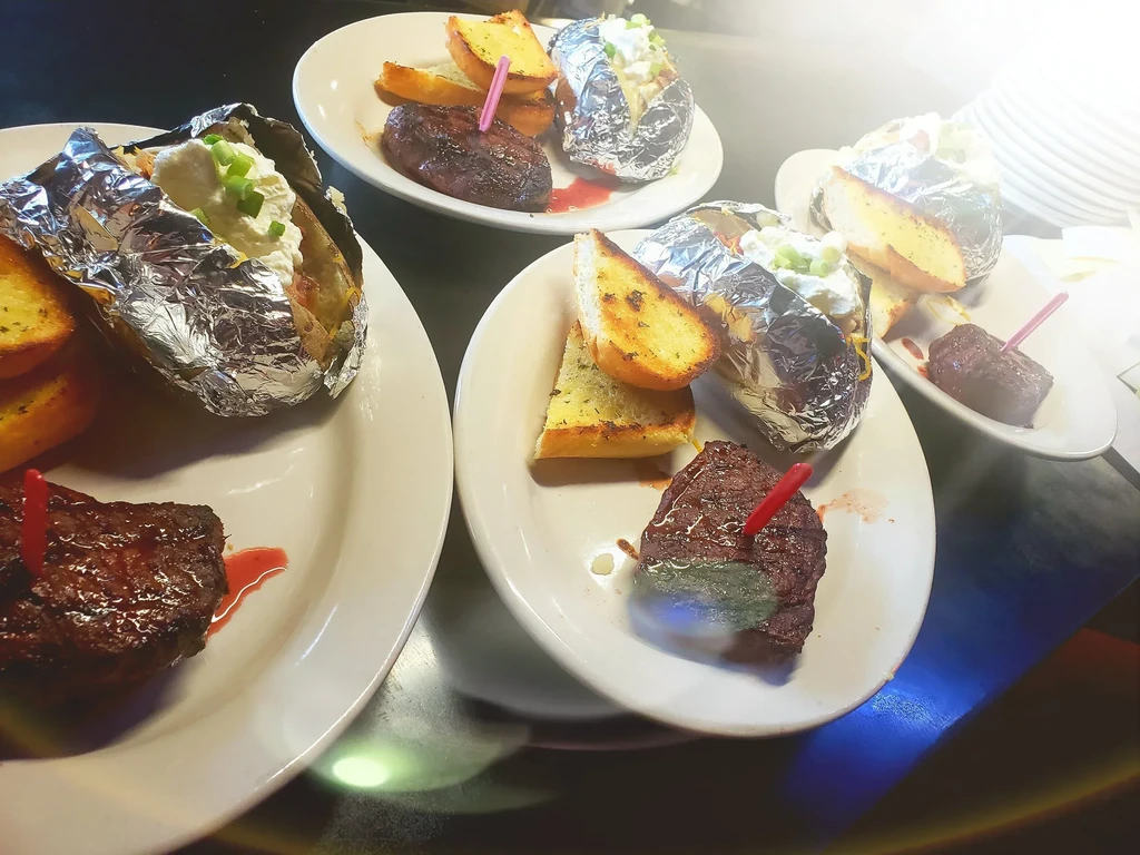 Restaurant plates with grilled steak, baked potato, and garlic bread.