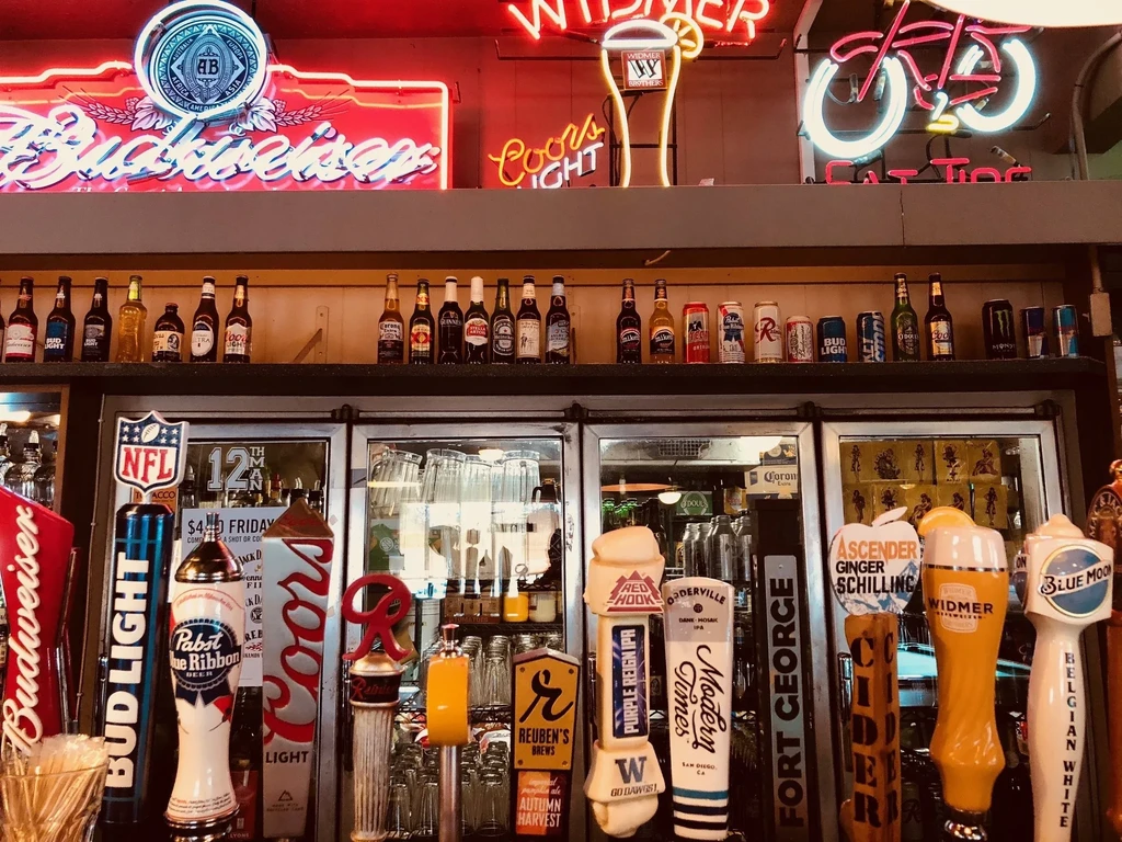 Bar counter with many beer taps, bottles, cans, and neon signs.